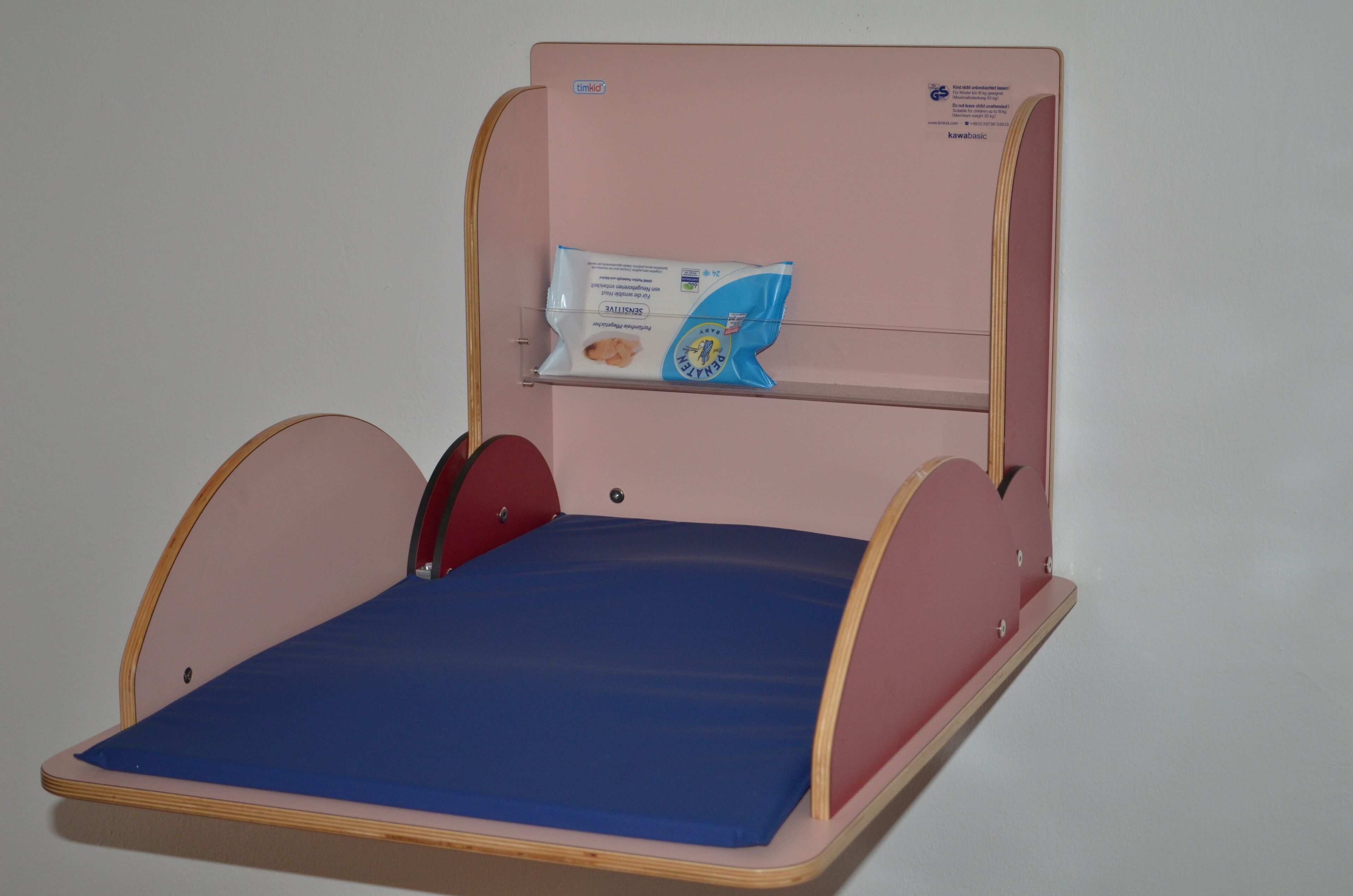 Un lit pour enfants avec un matelas bleu, une étagère au-dessus pour le rangement et une barrière latérale rouge.
