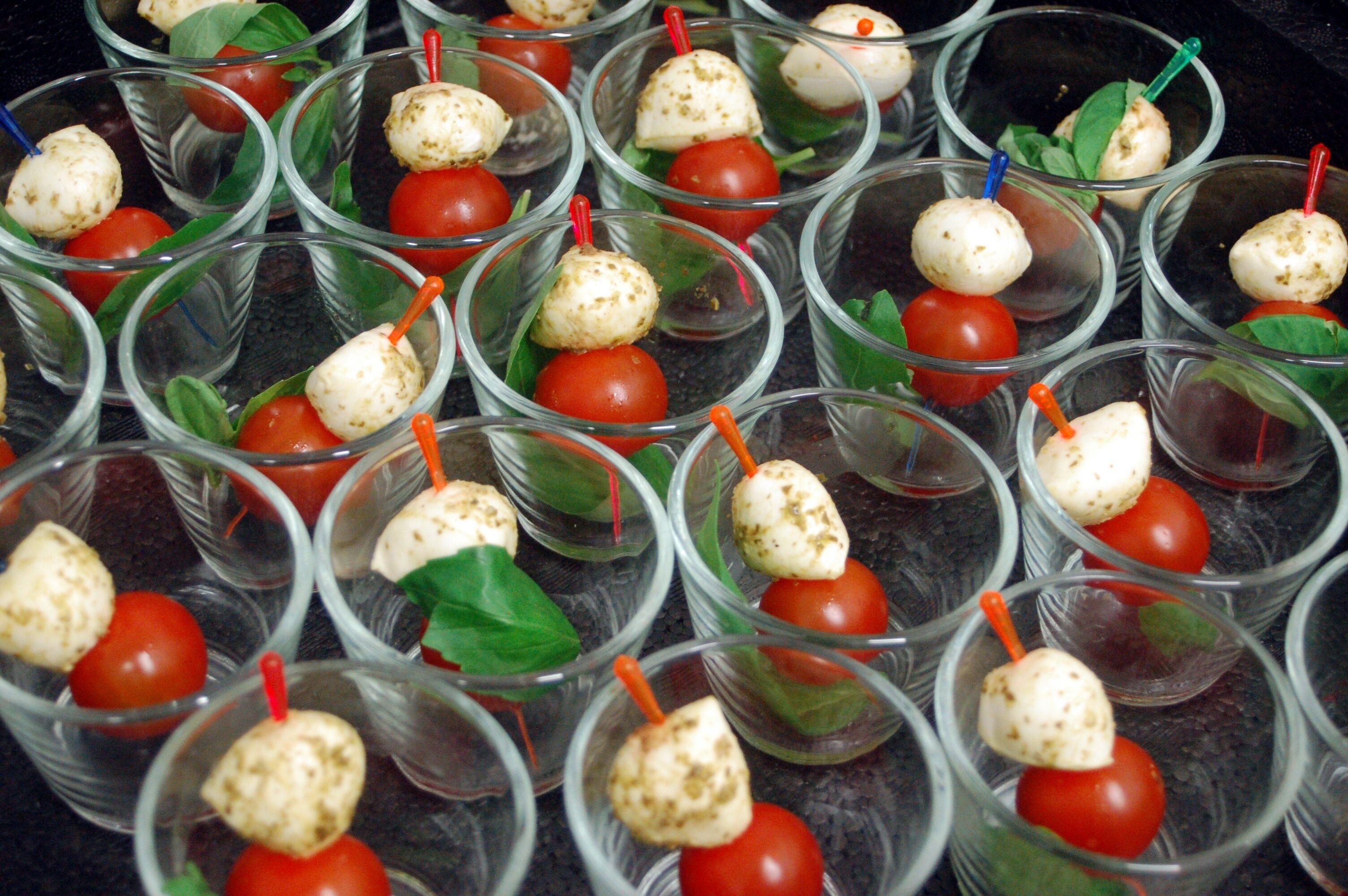 Multiple clear glasses containing a food item with a red spherical object and a white spherical object, each with a colored stick.
