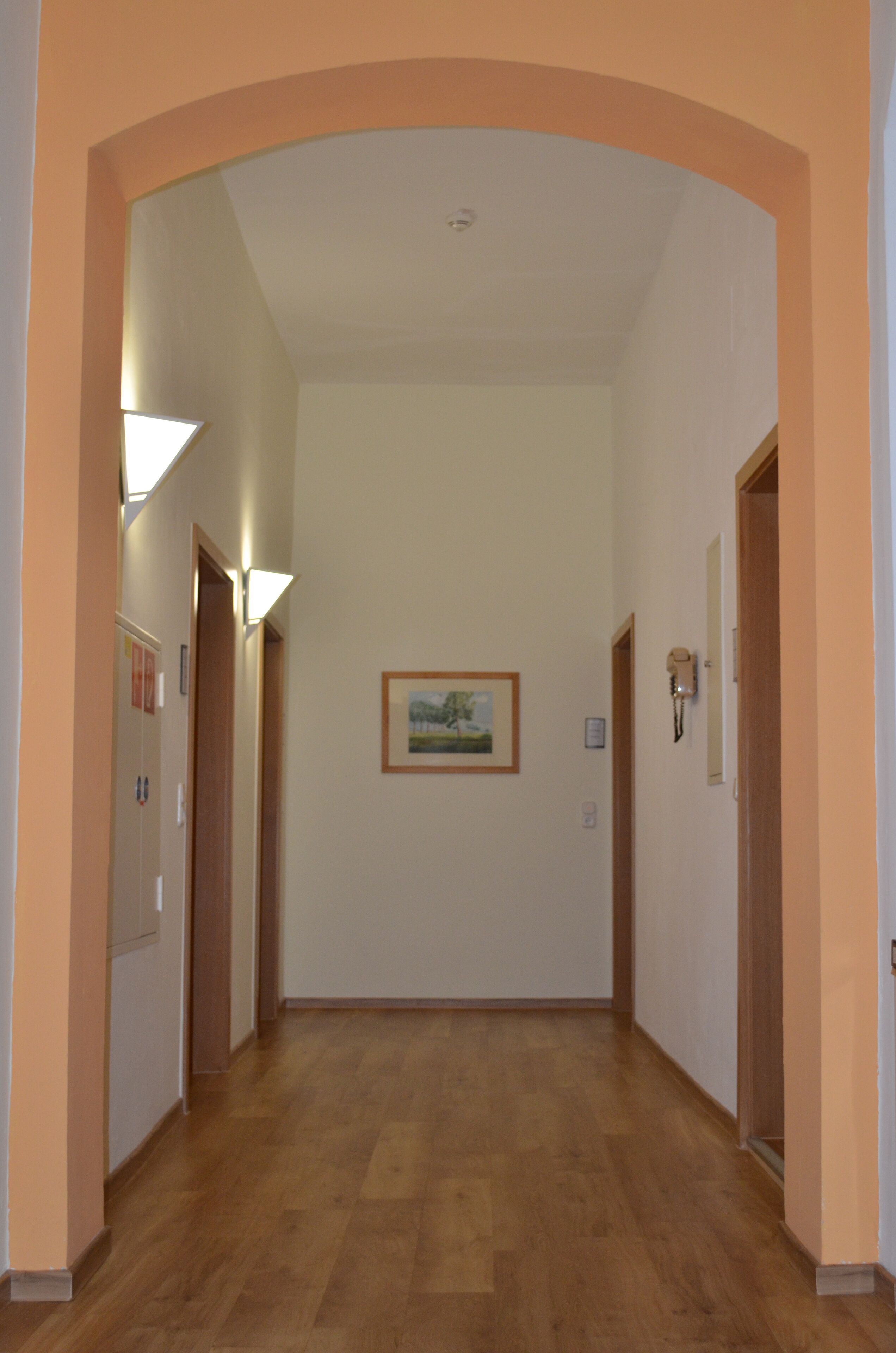 Ein Flur mit Holzdielenboden, einem gerahmten Bild an der Wand und einer Tür rechts.