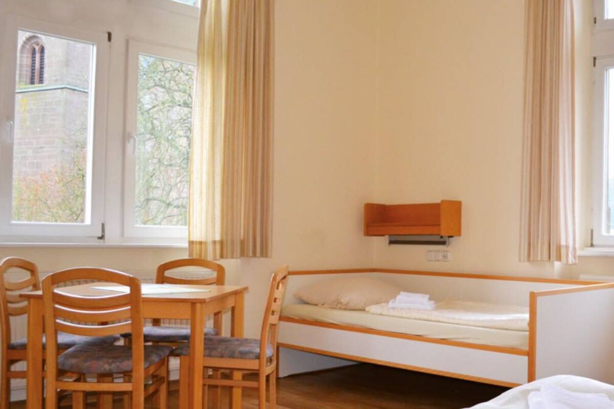 A room with a bunk bed, a wooden table with chairs, and a window with curtains.