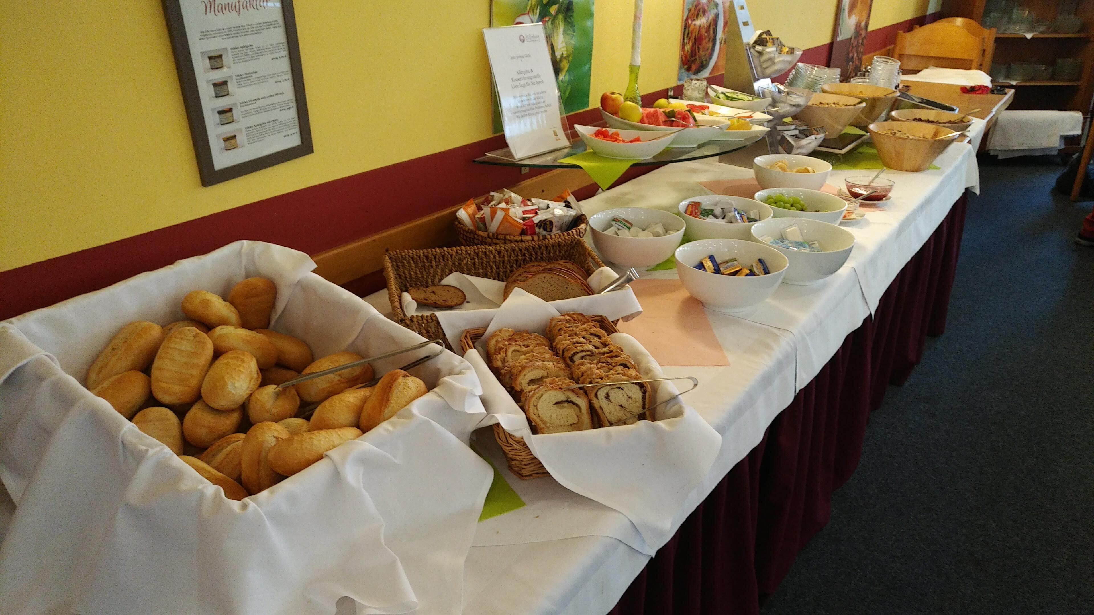 A buffet table with various food items including bread, pastries, and bowls of fruits and vegetables.