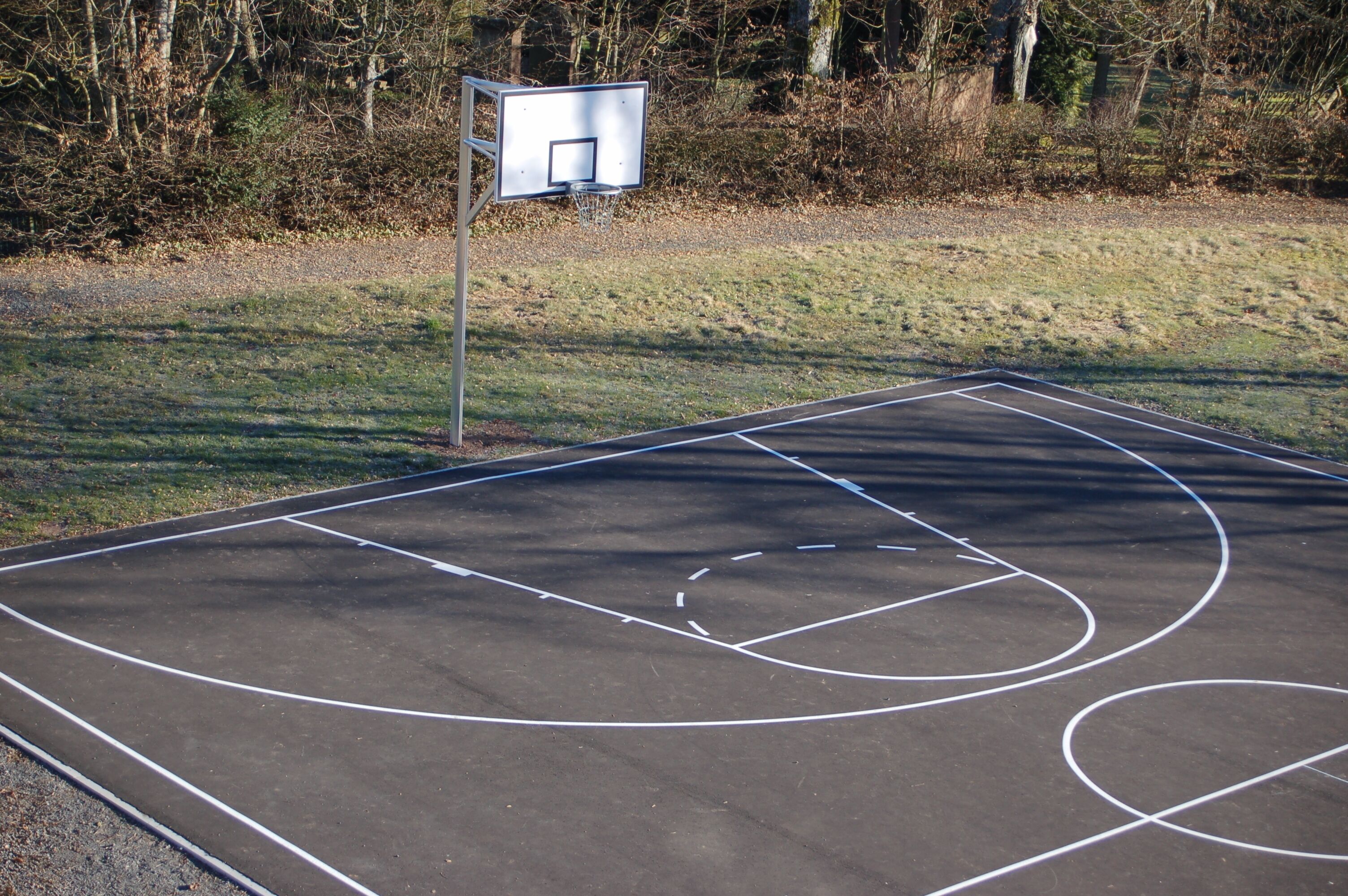 An outdoor basketball court with a metal basketball hoop and a net.