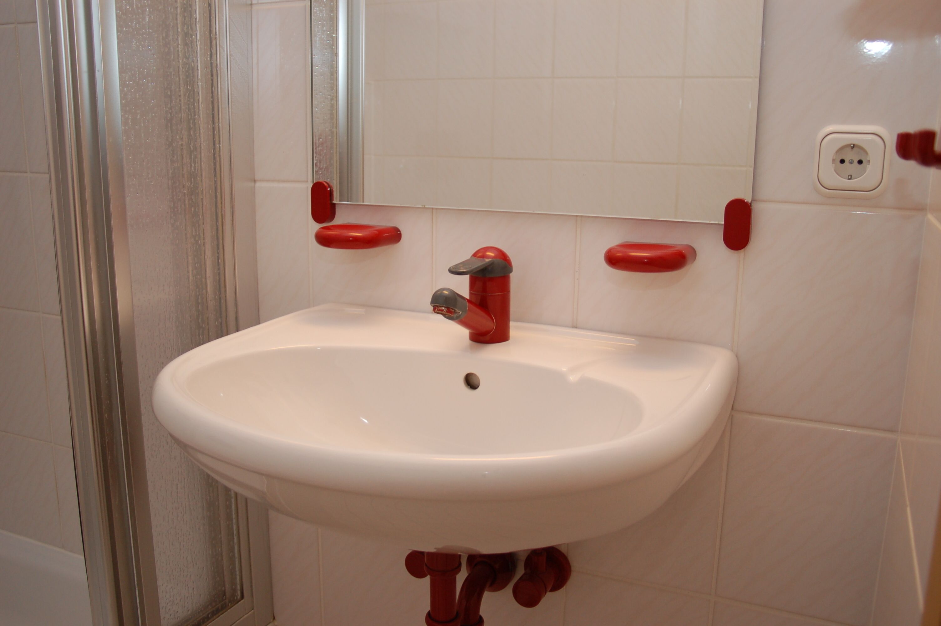 Un baño con lavamanos blanco, grifo rojo y dispensadores de jabón rojos.