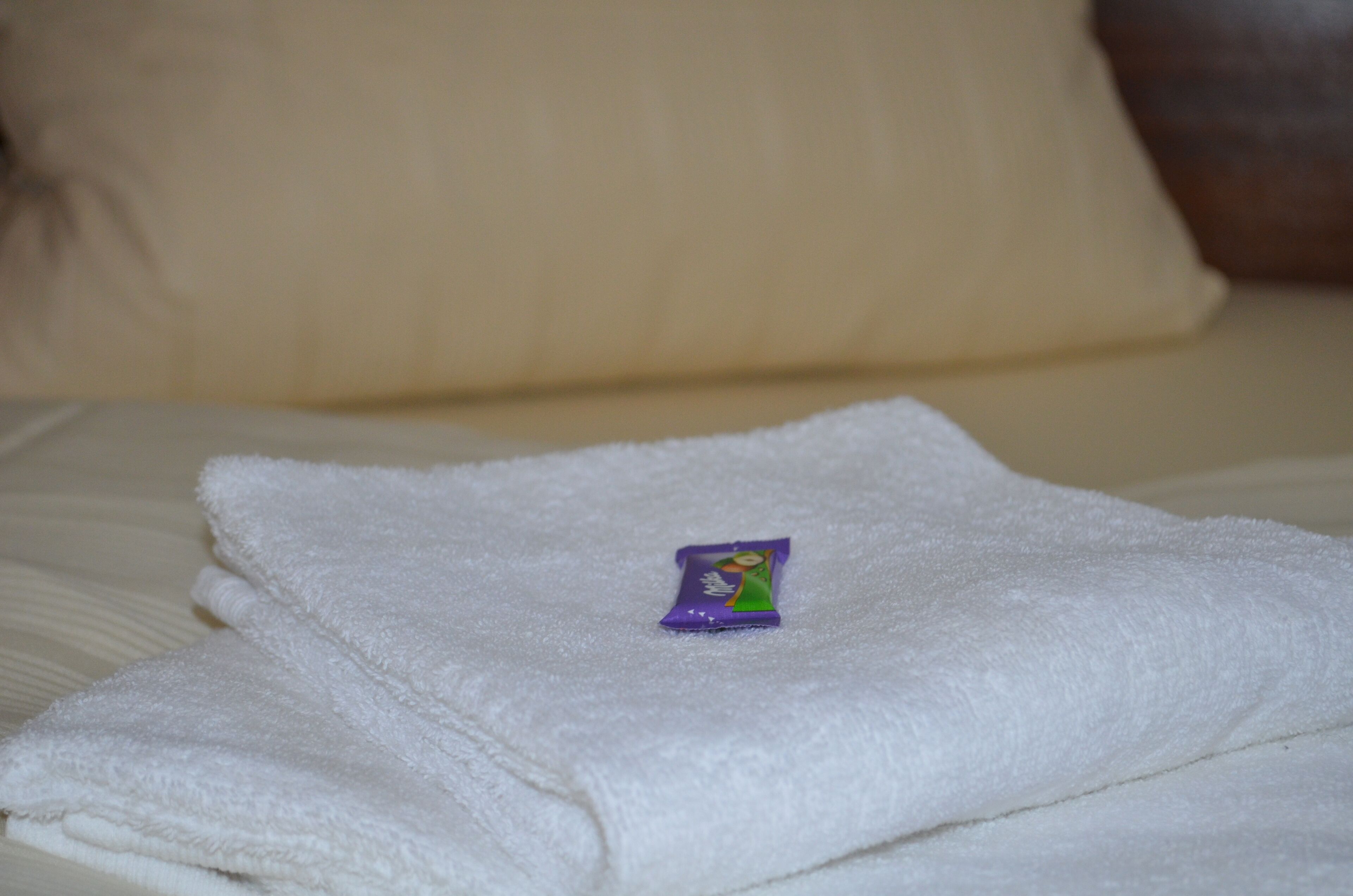 Una toalla blanca doblada ordenadamente sobre una cama con un almohadón.