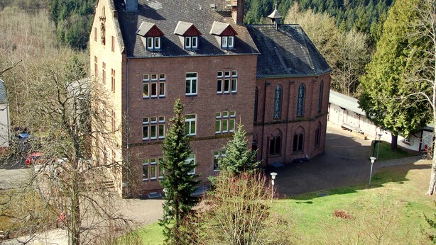 A large, historic building with multiple windows and a prominent tower, surrounded by trees and a hilly landscape. - Stiftsberg Bildungs und Freizeitzentrum (Kyllburg)