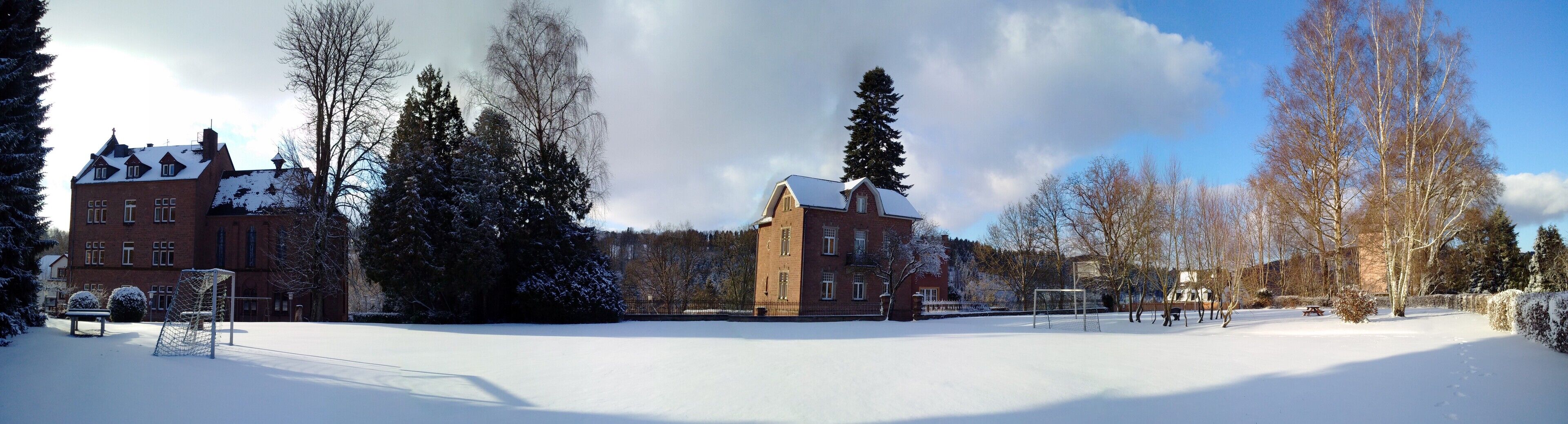 Un patio cubierto de nieve con un edificio de ladrillo, un arco de fútbol y una mesa de picnic.