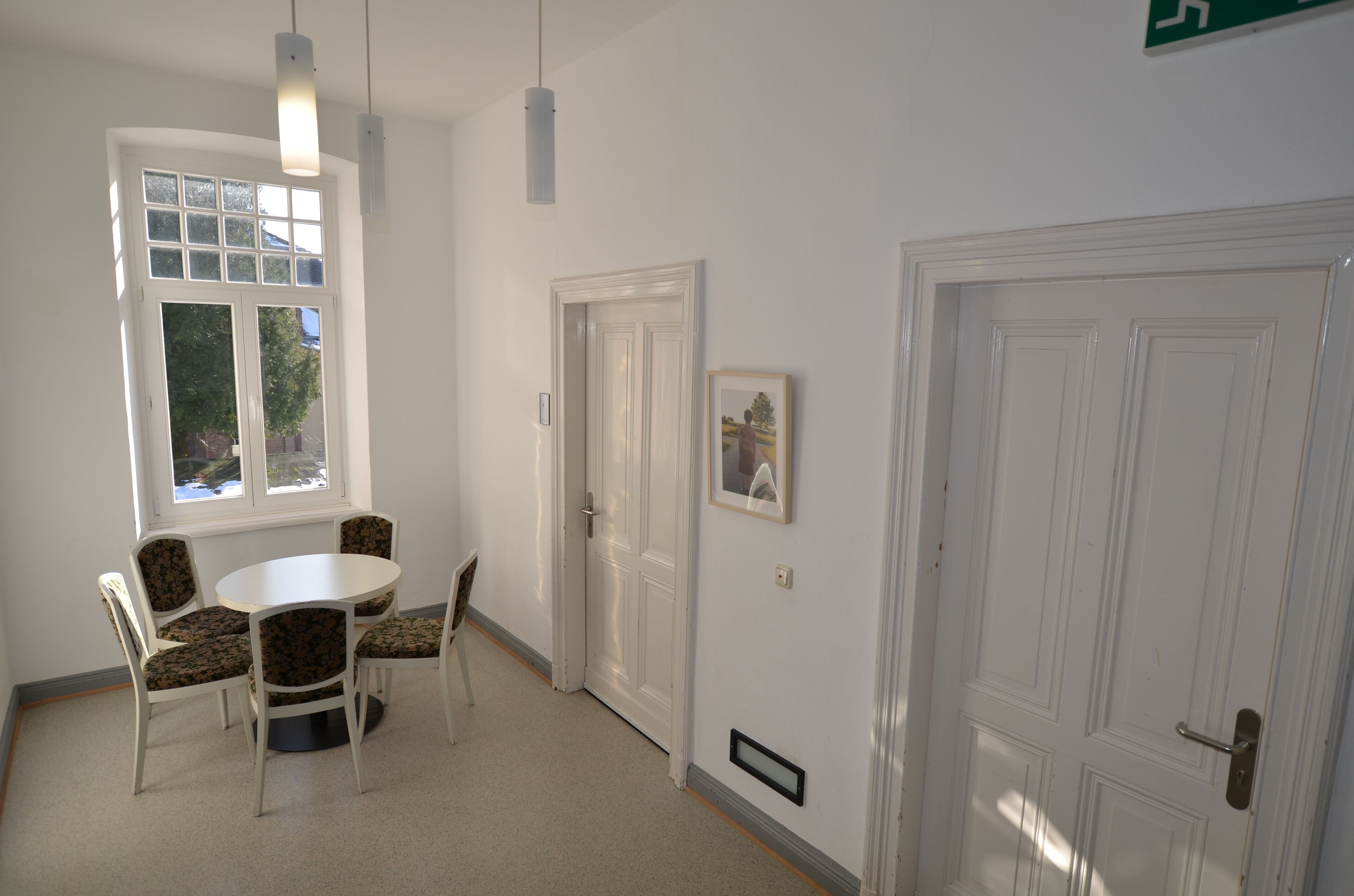 Una habitación con una mesa redonda y cuatro sillas, una ventana con vistas y dos puertas.