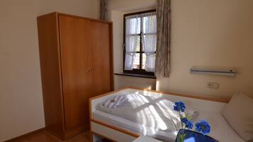 A hotel room with a bed, a wardrobe, a table with a bottle and glasses, and a window with curtains.