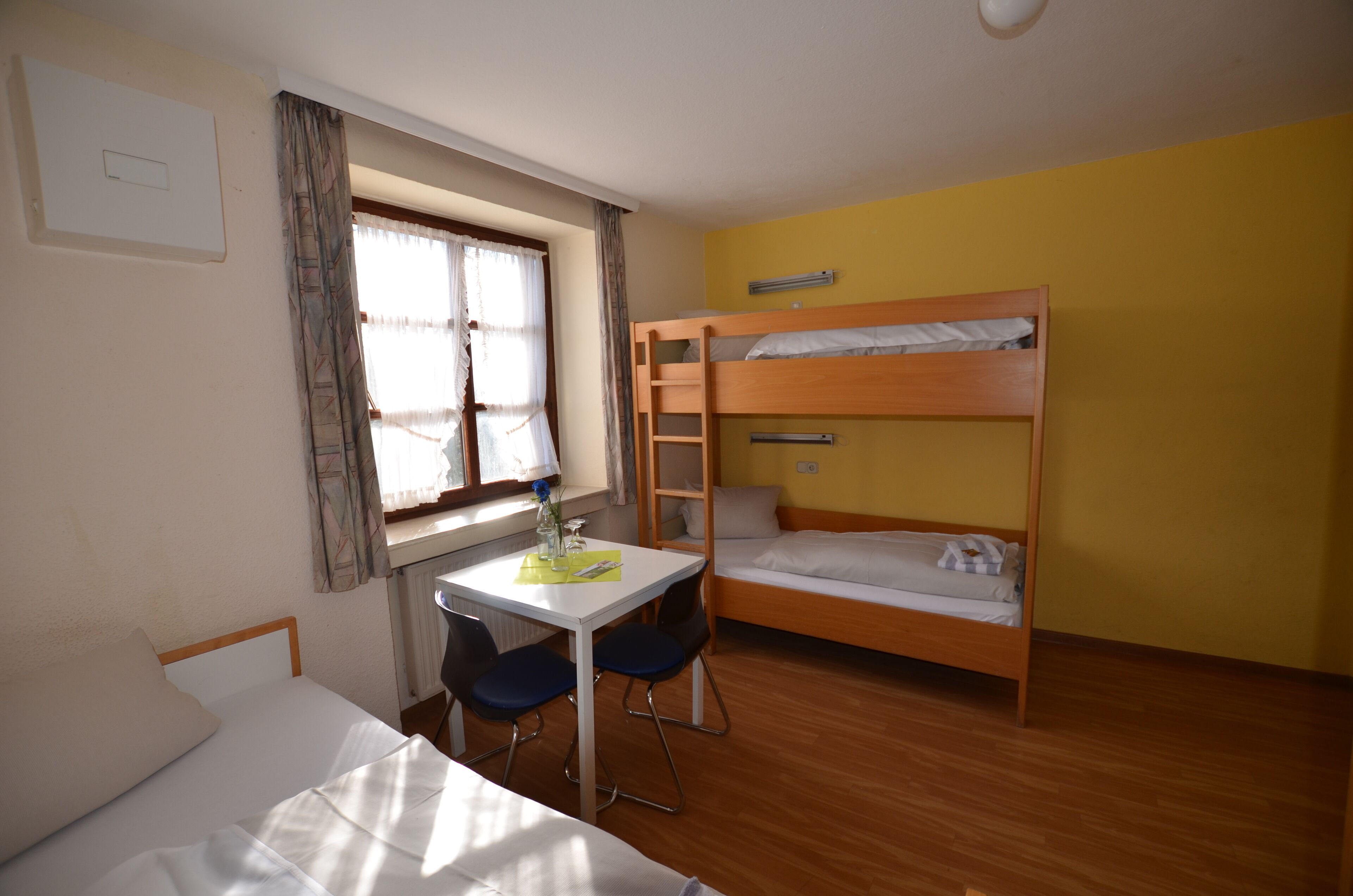 Una habitación con una cama litera, un escritorio con dos sillas, una ventana con cortinas y un radiador.