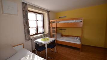 Una habitación con una cama litera, un escritorio con dos sillas, una ventana con cortinas y un radiador.