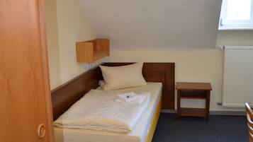 A bedroom with a single bed, a bedside table, a small wooden nightstand, a radiator, and a window with natural light.
