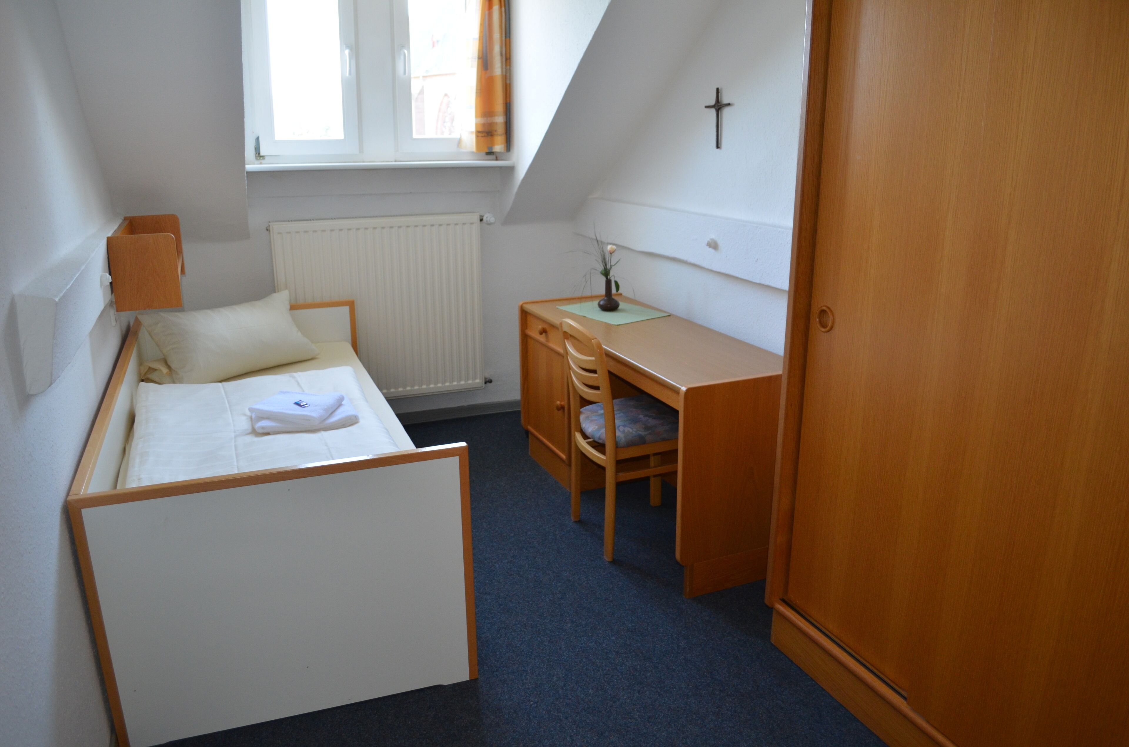 Ein kleiner, ordentlicher Raum mit einem Bett, einem Schreibtisch und einem Kleiderschrank.