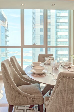 Comedor con una mesa redonda dispuesta para seis personas, ventanas amplias y vistas a edificios altos.