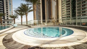 Ein kreisförmiger Pool mit einer zentralen Wasserspülung, umgeben von Palmen und hohen Gebäuden.