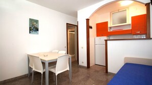 A compact room with a dining table and chairs, a kitchenette with orange cabinets, and a bed with a blue mattress. - Lovely apartment for 6 people with A/C, TV, terrace and pets allowed (San Michele Al Tagliamento)