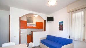 A compact kitchenette with a stove, oven, and microwave. There is a blue sofa and a small table with chairs. - Lovely apartment for 6 people with A/C, TV, terrace and pets allowed (San Michele Al Tagliamento)