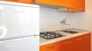 A kitchen with white appliances, orange cabinets, and a white tiled backsplash. - Lovely apartment for 6 people with A/C, TV, terrace and pets allowed (San Michele Al Tagliamento)