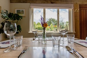 Una mesa de comedor dispuesta con copas de vino, copas de agua y cubiertos, con un jarrón de flores en el centro.