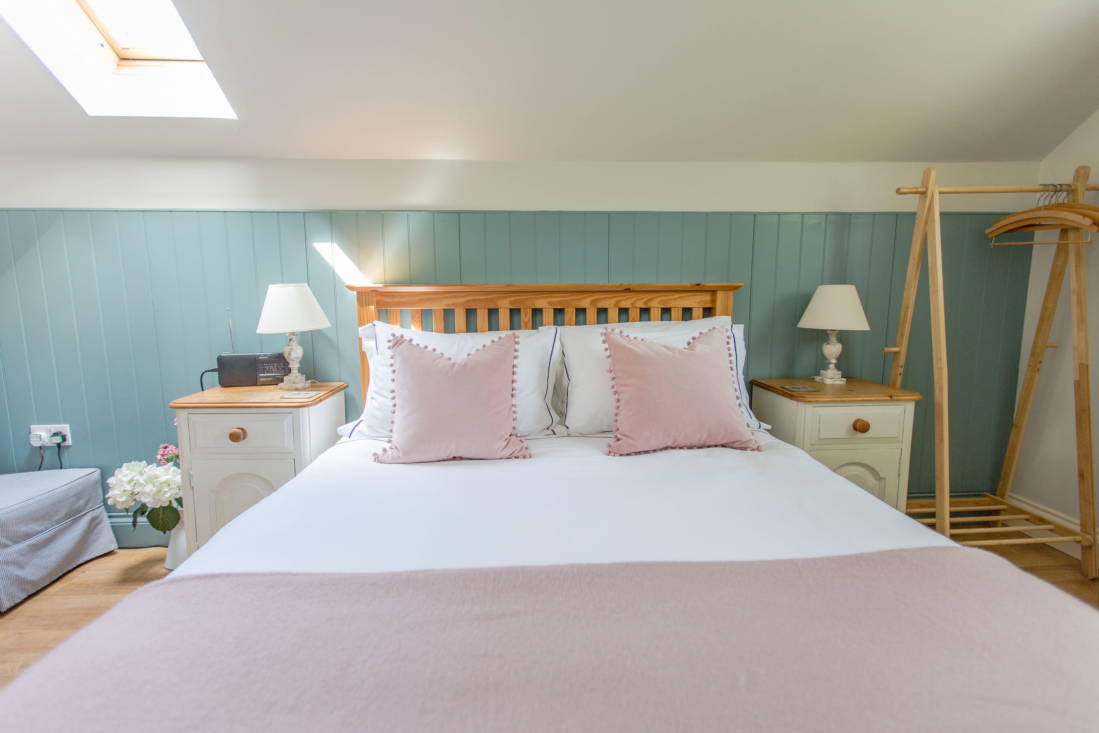 Une chambre à coucher comprenant un lit, deux tables de chevet, une commode, un porte-manteau en bois et une lucarne.
