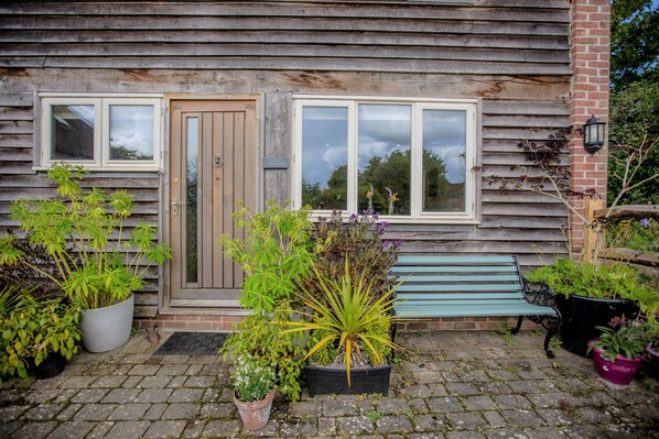 Una casa de madera con puerta principal, dos ventanas y un banco en el exterior.