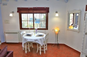 A dining area with a table set for two, a radiator, a window with a view, and a mirror on the wall.