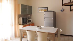 A small, modern kitchen with a dining table, four chairs, a refrigerator, a microwave, and a television.