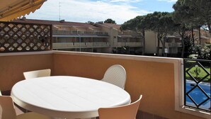 A patio with a round table and chairs, a view of neighboring buildings, and a pool in the background.