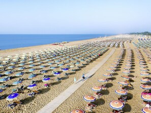 A beach with rows of umbrellas and chairs, a wooden walkway, and the ocean in the background.