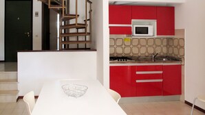 Una cocina con armarios rojos, un microondas blanco y una zona de comedor con una mesa blanca.