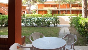 Un espace patio avec une table ronde et quatre chaises, entouré de verdure et, en arrière-plan, un bâtiment aux murs orange.