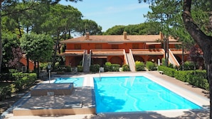 Un complexe hôtelier doté d’une piscine, d’un patio couvert et d’un bâtiment surmonté d’un toit en tuiles.