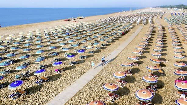 A beach with rows of umbrellas and chairs, a wooden walkway, and the ocean in the background. - Beautiful apartment for 6 people with A/C, pool, WIFI, TV, balcony and pets allowed (San Michele Al Tagliamento)