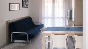 A small room with a bed, a table, and two chairs. There is a window with curtains, a television, and two framed pictures on the wall. - Beautiful apartment for 6 people with A/C, pool, WIFI, TV, balcony and pets allowed (San Michele Al Tagliamento)