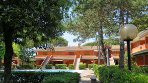 A pathway leading to a building with a tiled roof and arches, surrounded by lush greenery and a clear sky. - Beautiful apartment for 6 people with A/C, pool, WIFI, TV, balcony and pets allowed (San Michele Al Tagliamento)