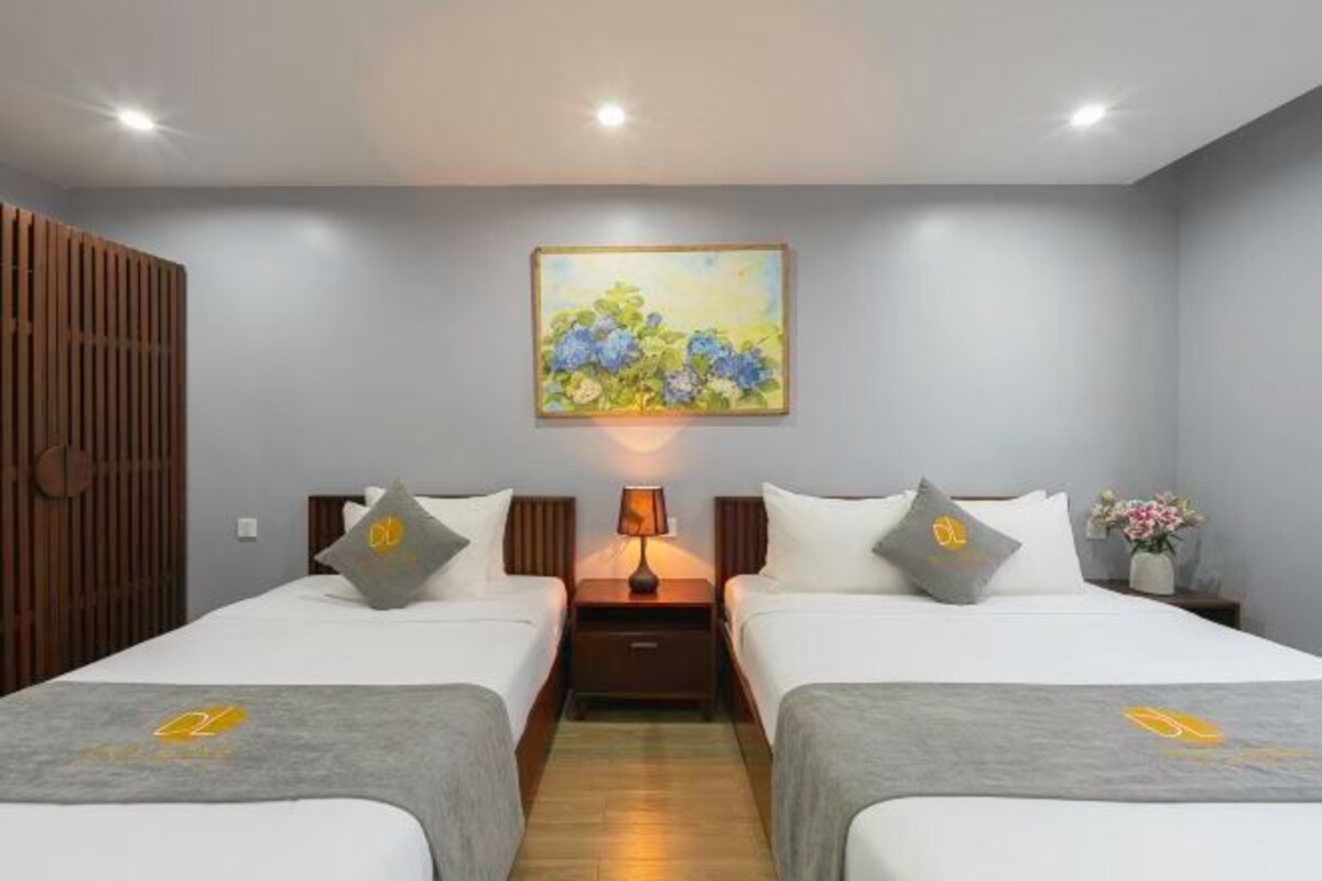A hotel room with two beds, a nightstand with a lamp, a painting on the wall, and a wooden partition.