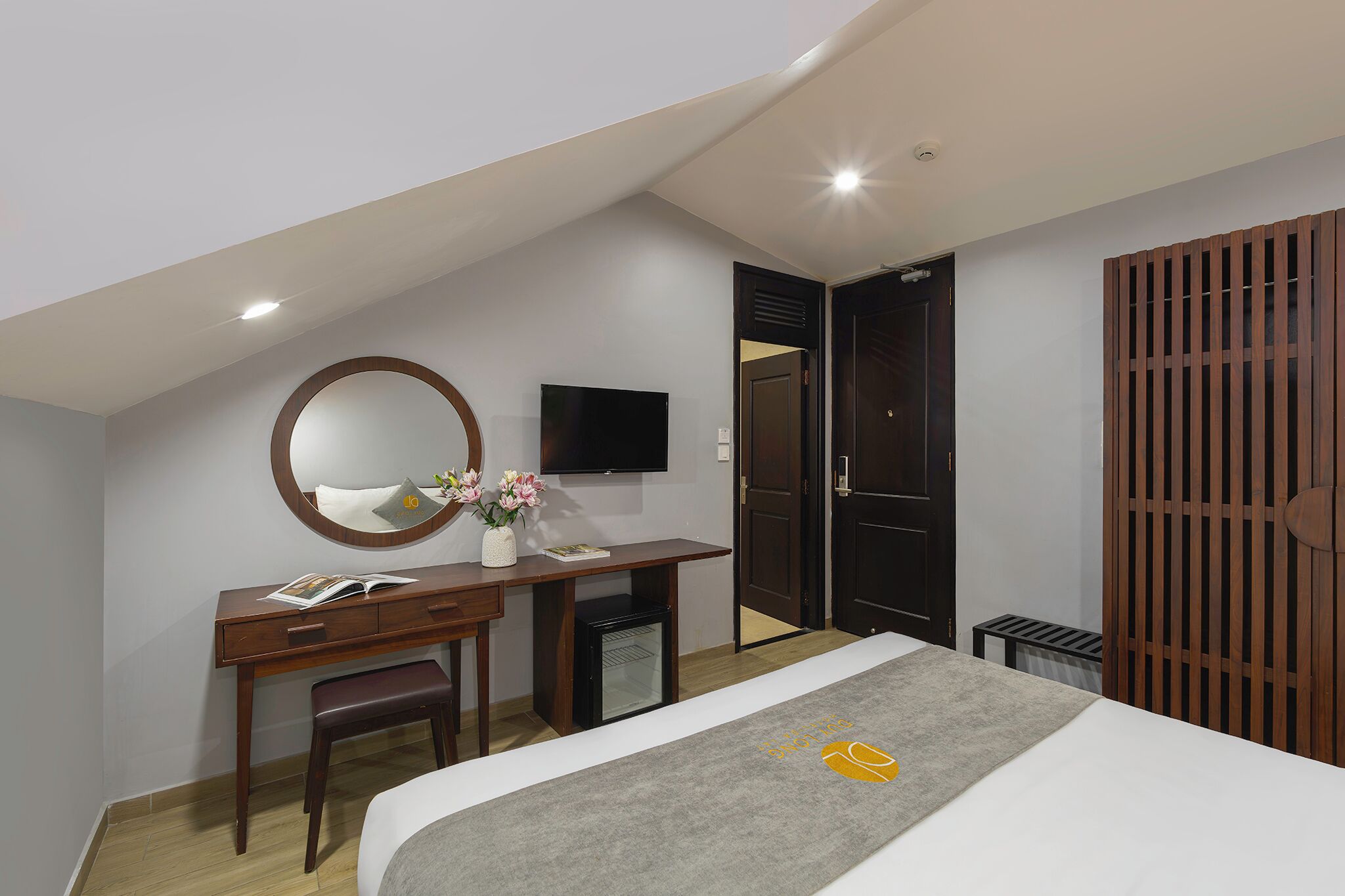 A hotel room with a bed, a desk with a chair, a small refrigerator, a TV, and a wardrobe.