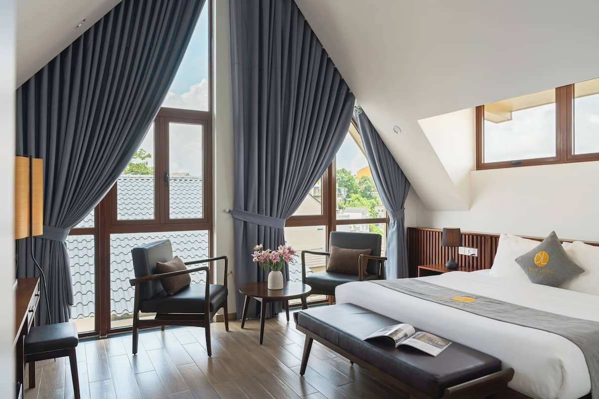 Ein Hotelzimmer mit einem Bett, zwei Stühlen, einem kleinen Tisch mit Blumen und einer Bank.