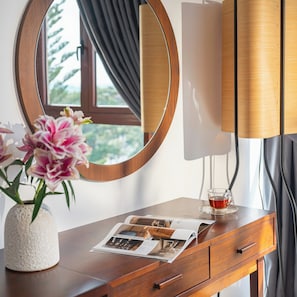 A wooden dresser with a round mirror, a vase with flowers, and a glass of tea. - Duy Long Hotel (Da Lat)