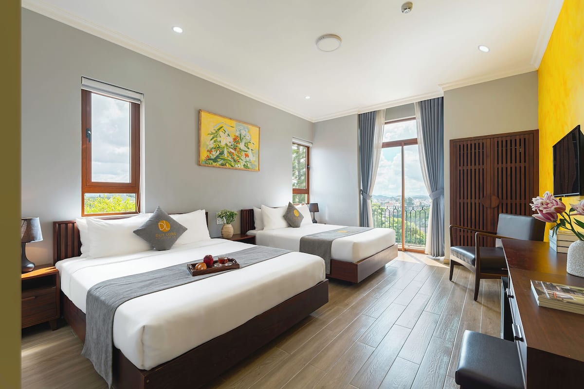 Ein Hotelzimmer mit zwei Betten, einem Schreibtisch, einem Stuhl, einem Fernseher und einem Balkon mit Blick.