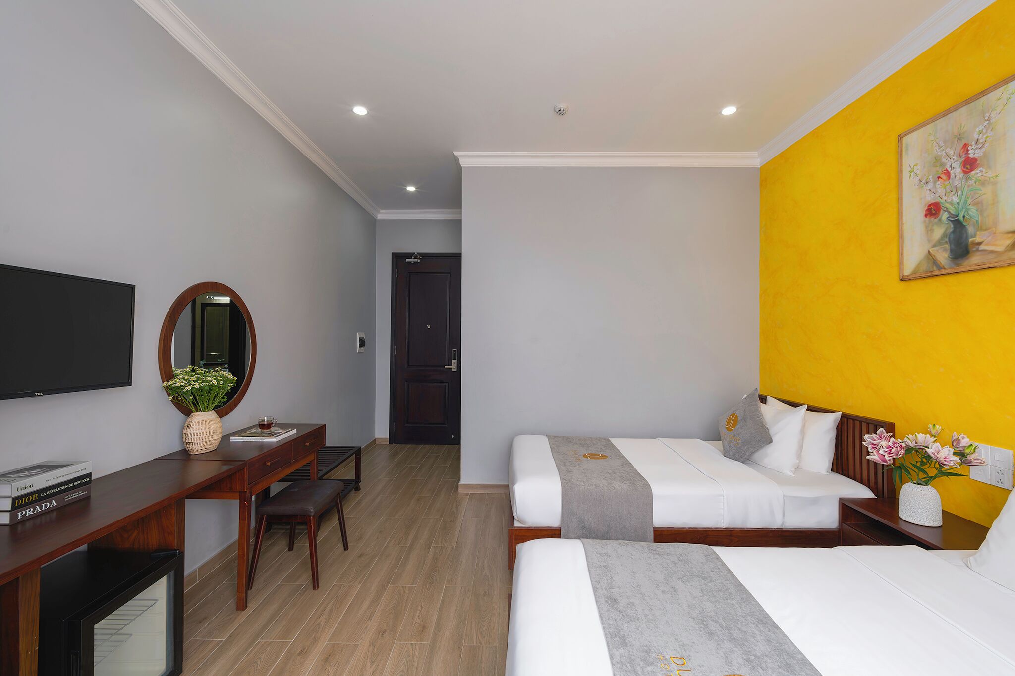 Quarto de hotel com duas camas, uma escrivaninha com espelho, televisão e um quadro na parede.