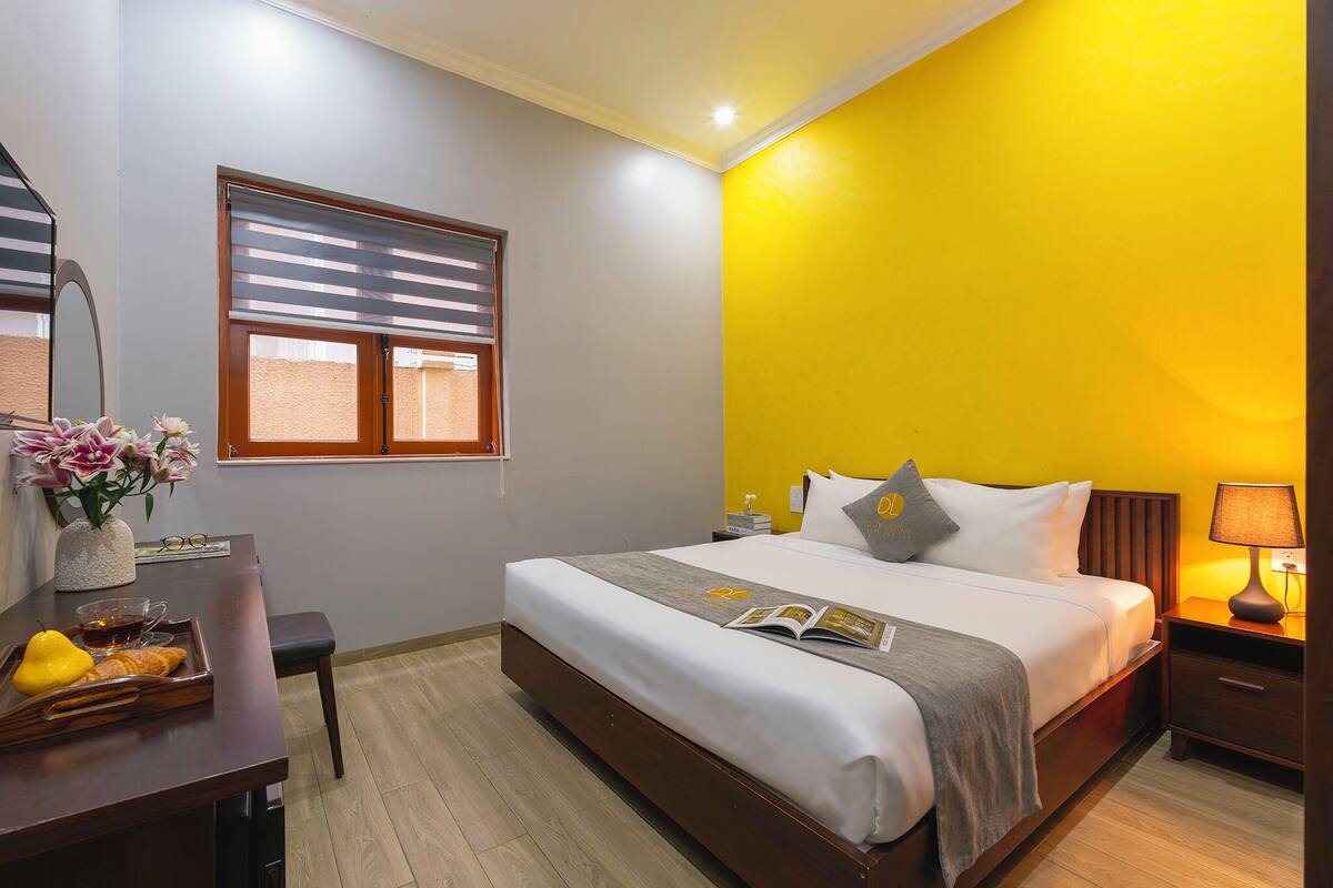 Ein Hotelzimmer mit Bett, Nachttisch, Lampe und einem Fenster mit Jalousien.