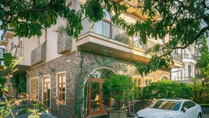 A white car parked in front of a building with a stone facade, a balcony, and a potted plant. - Duy Long Hotel (Xuan Huong - Da Lat)
