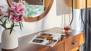 A wooden vanity with a round mirror, a vase with pink flowers, a glass of tea, and a magazine on the surface. - Duy Long Hotel (Xuan Huong - Da Lat)