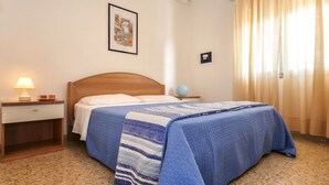Uma cama bem arrumada com um cobertor azul, uma luminária de cabeceira e um quadro na parede.