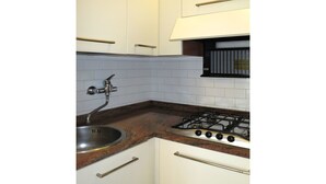 Uma cozinha pequena com armários brancos, uma pia de aço inoxidável, um fogão a gás e um revestimento de azulejos.