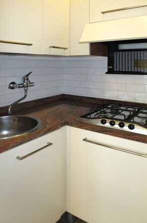 A small kitchen with white cabinets, a stainless steel sink, a gas stove, and a tiled backsplash.