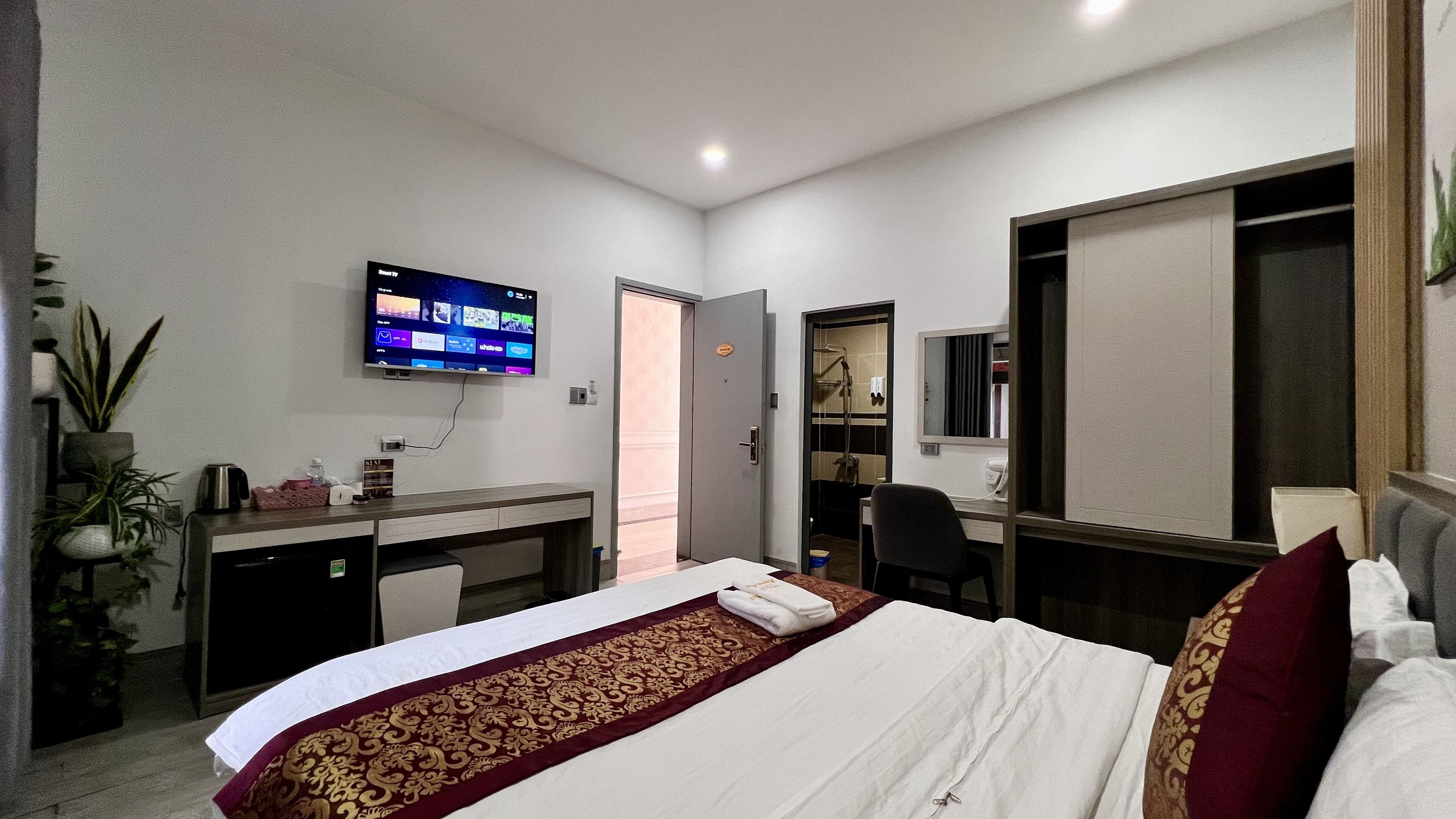 A hotel room with a bed, a desk, a television, a mirror, and a shower area.