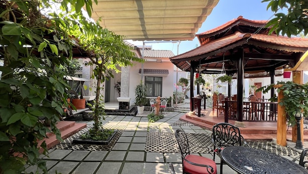 Un patio techado al aire libre con suelo de baldosas, arreglos de asientos y plantas en macetas.