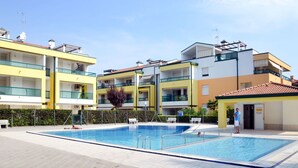 A modern hotel with a swimming pool, multiple balconies, and a clear blue sky. - Nice apartment for 4 guests with A/C, pool, TV and terrace (Bibione)