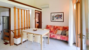 A dining area with a table and chairs, a sofa, and a kitchen area with a refrigerator. - Beautiful apartment in villa for 8 guests with A/C, pool, TV, terrace and pets allowed (San Michele Al Tagliamento)